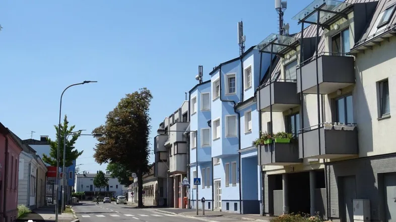 Blick auf eine Wohnstraße mit mehrstöckigen Gebäuden, blauen Fassaden und Balkonen unter klarem Himmel.