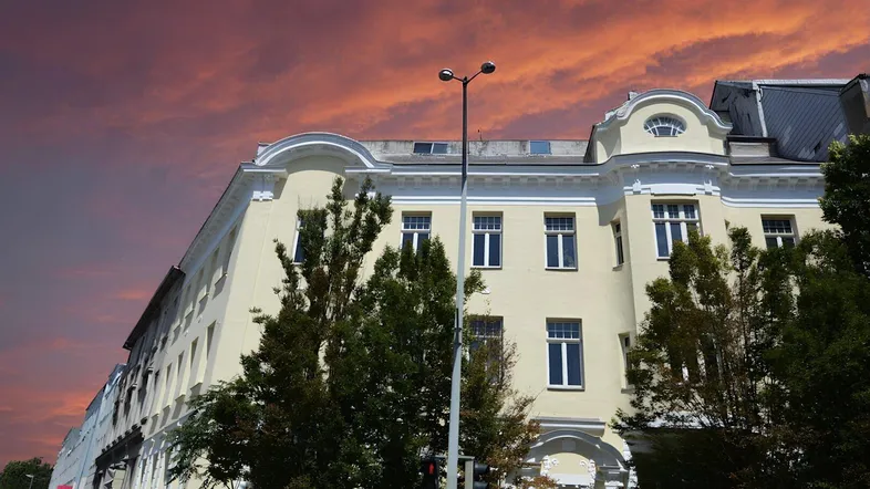 Historisches Gebäude mit heller Fassade und dekorativen Elementen unter einem dramatischen Abendhimmel.