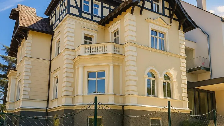 Historische Villa mit eleganter Fassade, Fachwerkdetails und gepflegtem Vorgarten unter blauem Himmel.