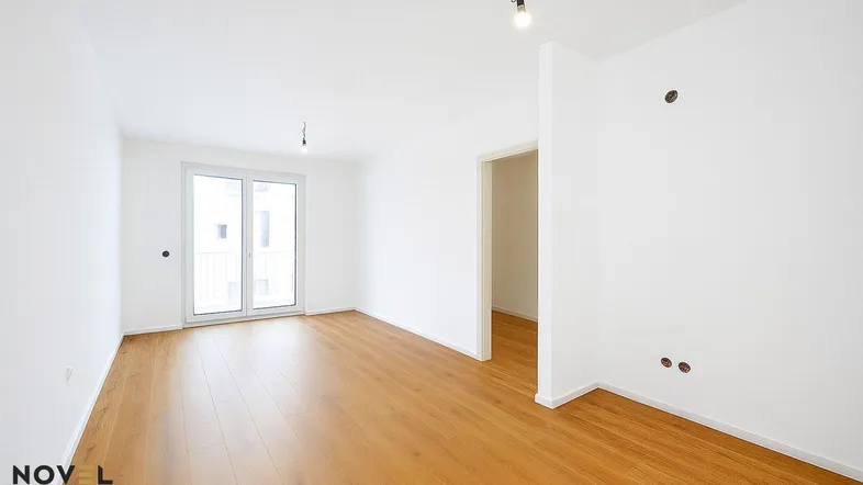 Helles, leeres Zimmer mit Holzboden und Zugang zu einem französischen Balkon.