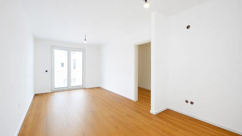 Helles, leeres Zimmer mit Holzboden und Zugang zu einem französischen Balkon, bereit zum Einzug.