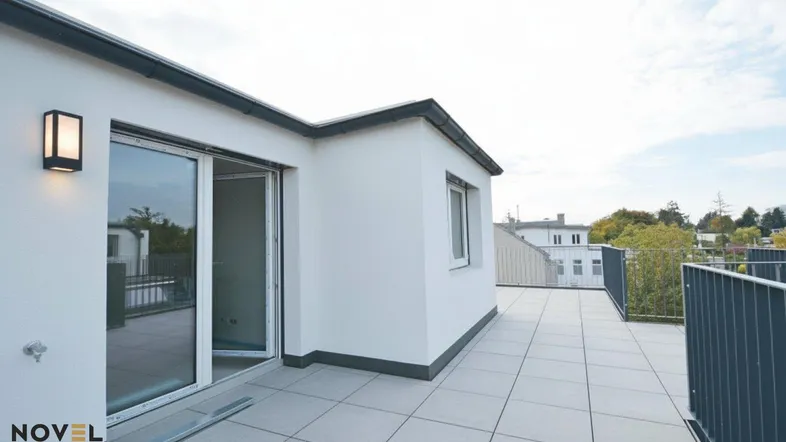 Große Dachterrasse mit Fliesenboden, Schiebetür und Blick auf die Umgebung.