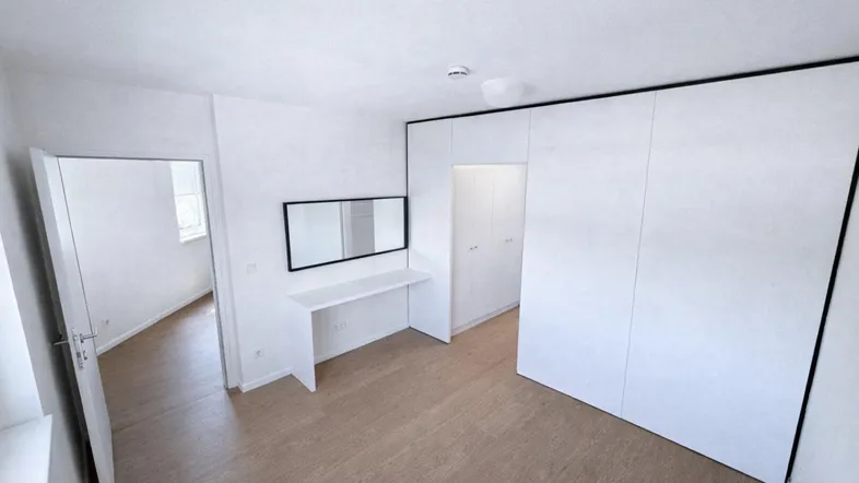 Schlafzimmer mit Laminatboden, integrierten Schränken und einem Schminktisch mit Spiegel.