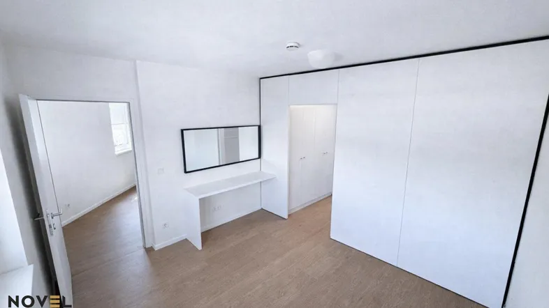 Helles Schlafzimmer mit integriertem Kleiderschrank, Schreibtisch und hellem Holzboden.