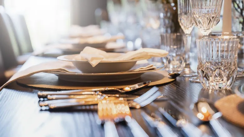 Ein elegant gedeckter Esstisch mit glänzendem Besteck und Kristallgläsern, bereit für eine festliche Mahlzeit.