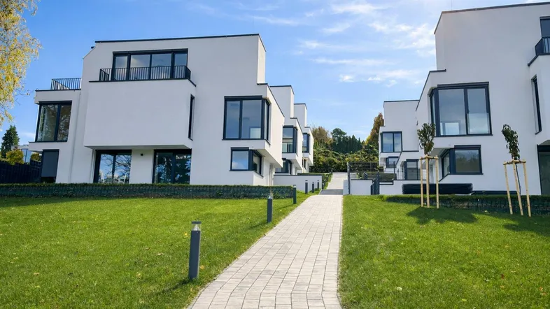 Moderne weiße Gebäude mit großen Fenstern und gepflegtem Rasen unter strahlendem Sonnenschein.