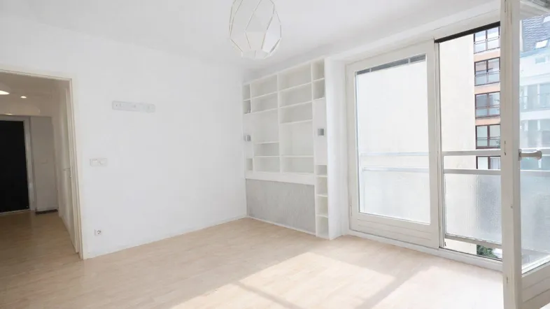 Helles, leeres Zimmer mit Einbauregal und Zugang zu einem Balkon.