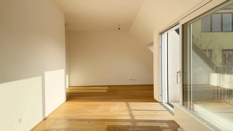 Heller Wohnraum mit Holzboden, Dachschrägen und Zugang zu einer sonnigen Terrasse.
