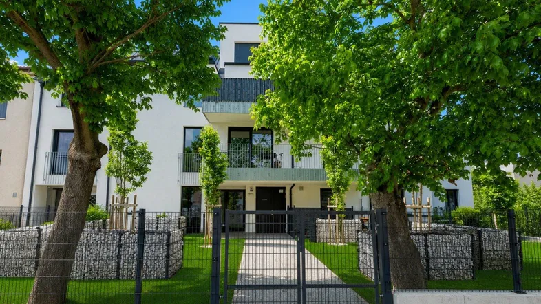 Moderne Wohnanlage mit weißer Fassade, Balkonen und gepflegter Grünfläche im Vorgartenbereich.