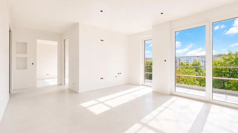 Helles, unmöbliertes Zimmer mit großen Fenstern, die viel Tageslicht hereinlassen und einen Blick ins Grüne bieten.