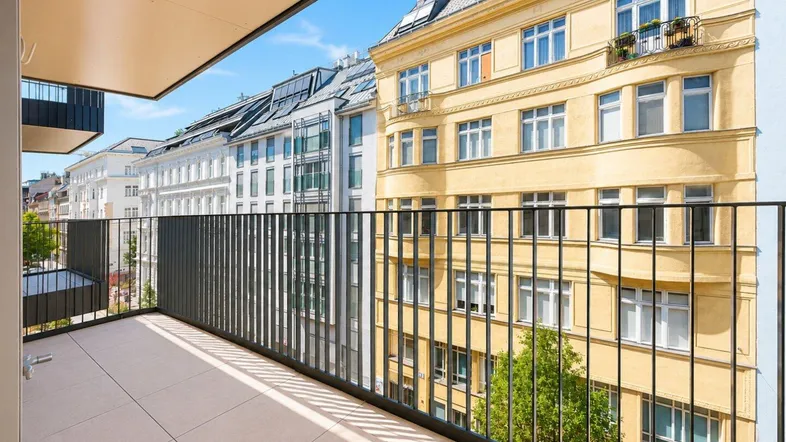 Geräumiger Balkon mit Fliesenboden und Blick auf die umliegenden Stadtgebäude und den blauen Himmel.