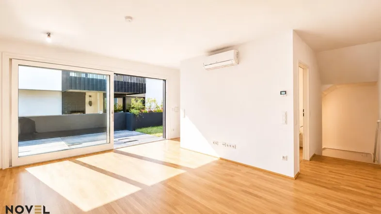 Helles Wohnzimmer mit Holzboden, großen Schiebetüren und Zugang zu einem Außenbereich.