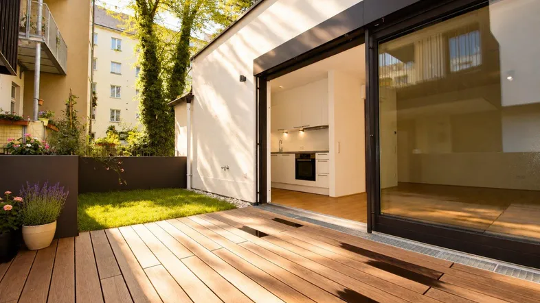Geräumige Terrasse mit Holzboden und direktem Zugang zur Küche, umgeben von Grünflächen.