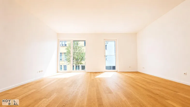Heller, leerer Raum mit Holzboden und großen Fenstern, die viel Tageslicht hereinlassen.