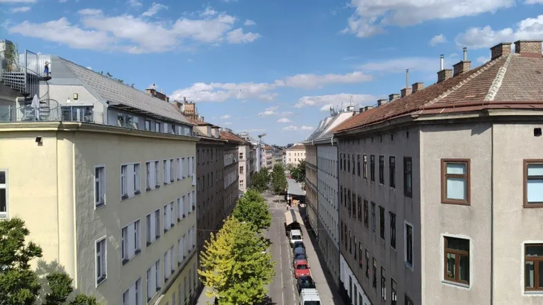 Blick von oben auf eine belebte Stadtstraße mit historischen Gebäuden und Bäumen.