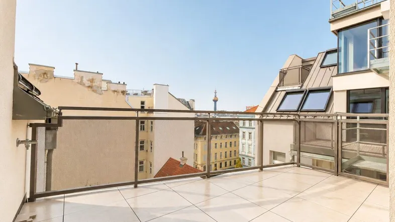 Geräumige Dachterrasse mit modernen Fliesen, Glasgeländer und weitem Blick über die Stadt.