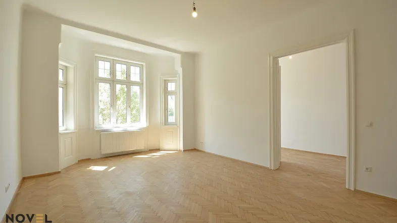 Helles, leeres Wohnzimmer mit Fischgrätparkett und großen Fenstern, bereit zur individuellen Gestaltung.