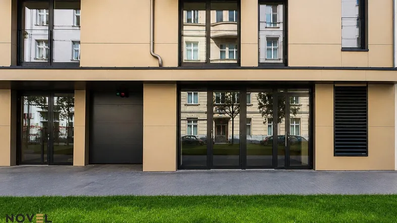 Moderne Fassade eines Wohngebäudes mit großen Fenstern, Garagentor und gepflegtem Vorgarten.