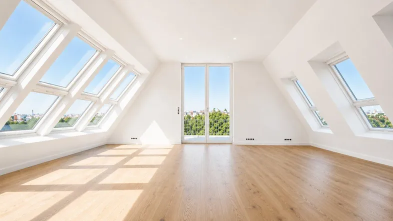 Helles Dachgeschosszimmer mit vielen Fenstern, Holzboden und Zugang zu einem Balkon.