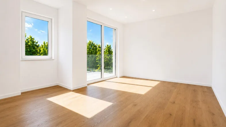 Helles Zimmer mit Holzboden und Zugang zu einem Balkon, bietet viel natürliches Licht.