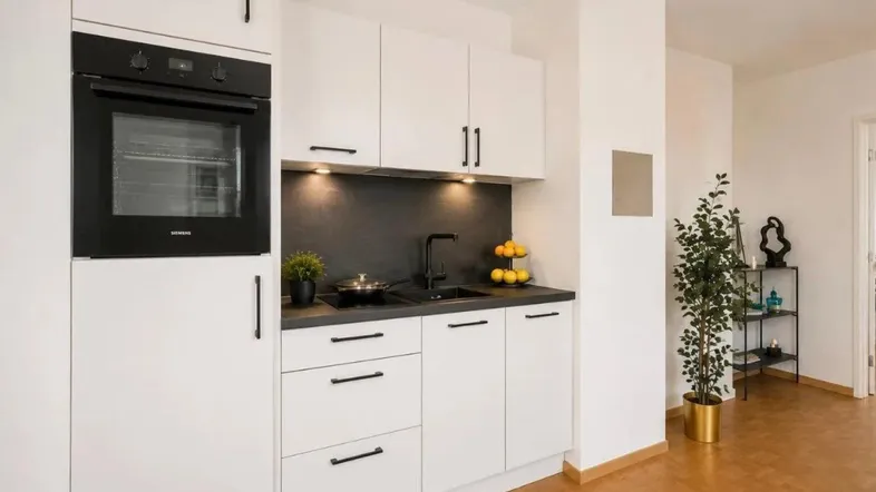 Moderne weiße Küche mit schwarzen Geräten, Parkettboden und integriertem Backofen.