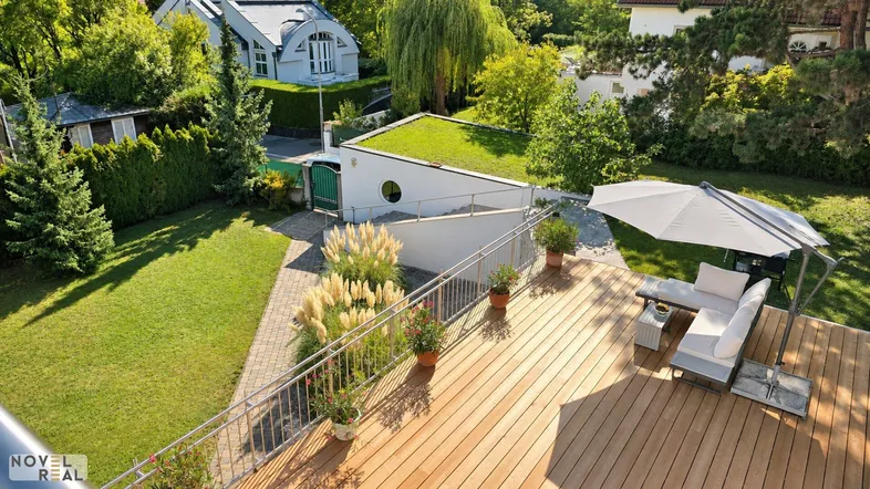 Große Holzterrasse mit bequemen Gartenmöbeln und Sonnenschirm, umgeben von viel Grün.