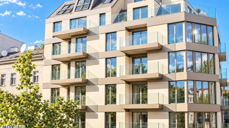 Modernes Mehrfamilienhaus mit zahlreichen Balkonen, großen Fensterfronten und Dachterrasse unter blauem Himmel.
