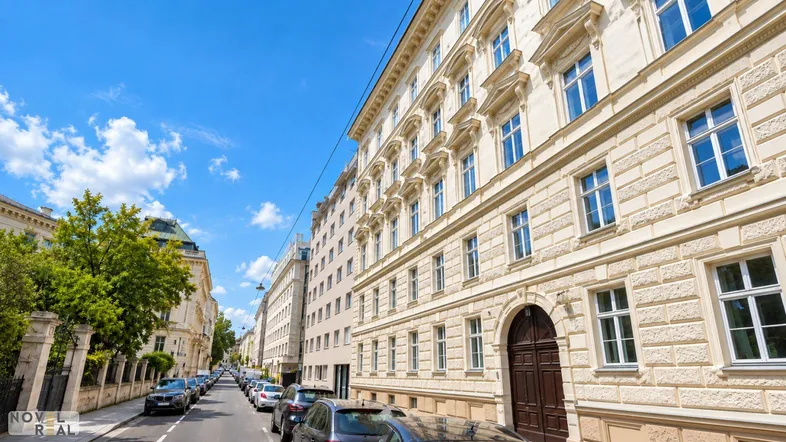 Historisches Gebäude in einer belebten Stadtstraße mit geparkten Autos und blauem Himmel.