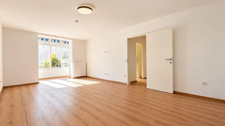 Helles, leeres Zimmer mit Laminatboden und großen Fenstern, bereit zur individuellen Gestaltung.