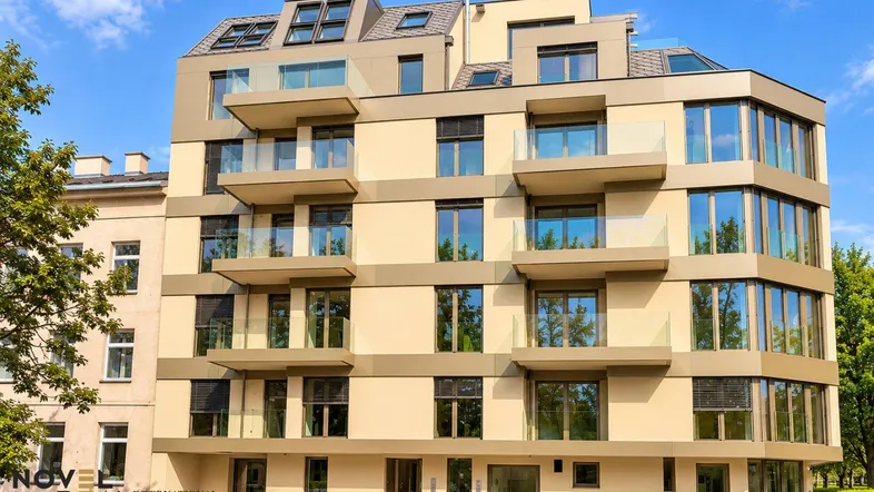 Modernes Mehrfamilienhaus mit mehreren Etagen, Balkonen und großen Fenstern unter blauem Himmel.