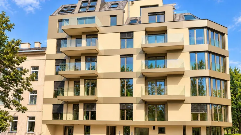 Modernes Mehrfamilienhaus mit mehreren Etagen, Balkonen und großen Fenstern unter blauem Himmel.