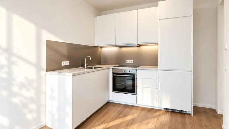Moderne Einbauküche in Weiß mit Holzboden und integrierten Geräten, bereit zur Nutzung.