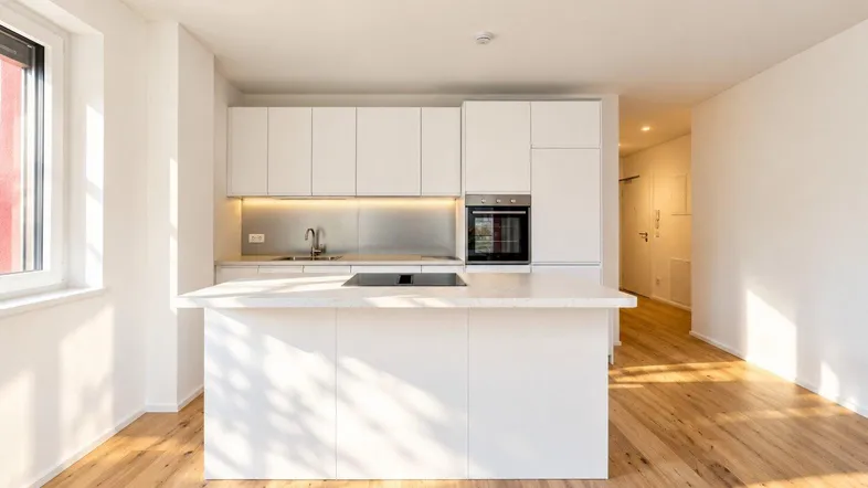Moderne, helle Küche mit weißer Kücheninsel, integrierten Geräten und Parkettboden.