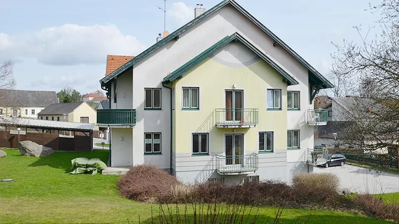 Mehrfamilienhaus mit mehreren Balkonen und einem gepflegten Vorgarten in ländlicher Umgebung.