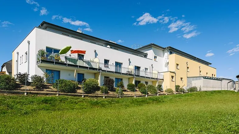 Modernes Mehrfamilienhaus mit Balkonen und gepflegter Grünfläche unter blauem Himmel.