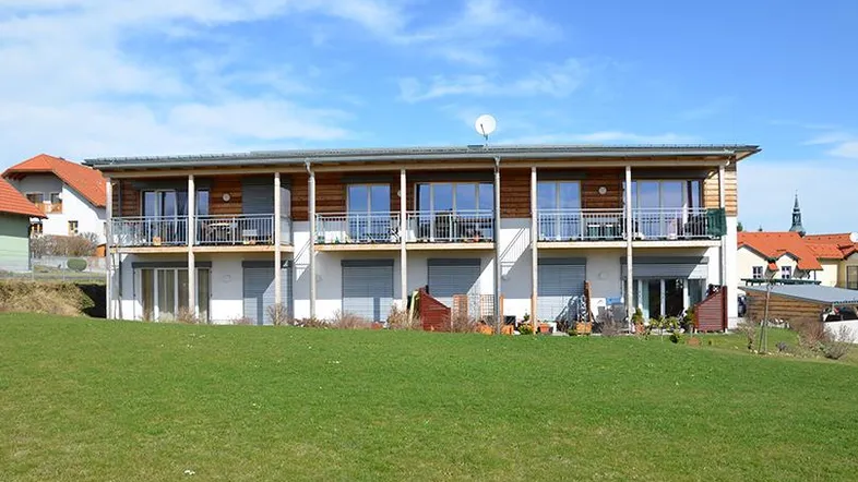 Modernes Mehrfamilienhaus mit Holzfassade, Balkonen und Blick ins Grüne auf einer Anhöhe.