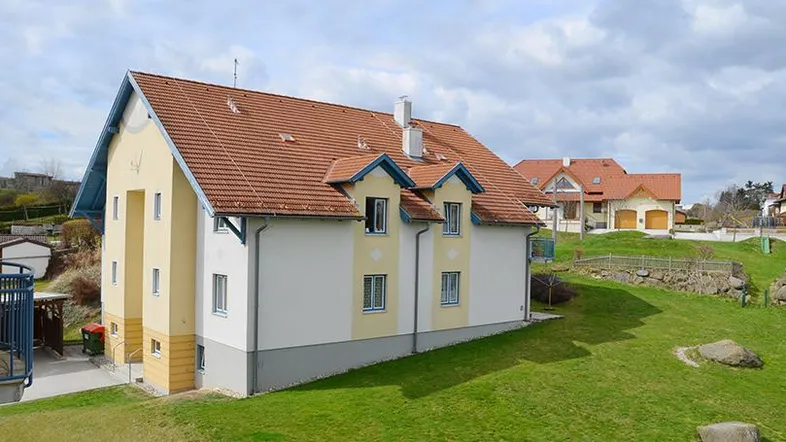 Ansicht eines gepflegten Einfamilienhauses mit gelber und weißer Fassade sowie rotem Ziegeldach in ländlicher Umgebung.