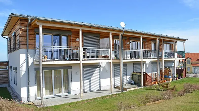 Modernes Mehrfamilienhaus mit Holzfassade, Balkonen und Terrassen, eingebettet in eine grüne Landschaft.