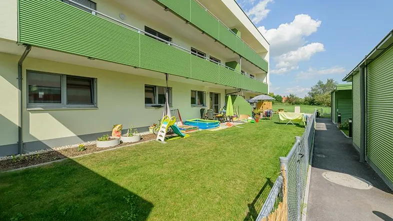 Moderne Wohnanlage mit grünen Balkonen und einem gepflegten Gartenbereich mit Spielgeräten.