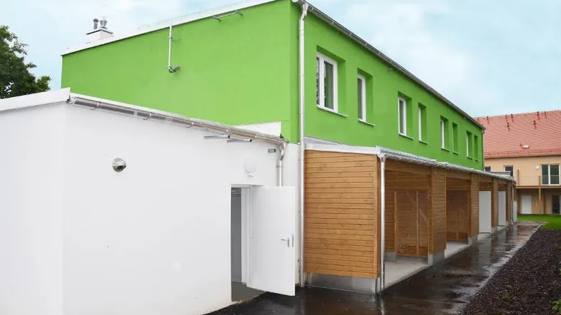Modernes Gebäude mit leuchtend grüner Fassade und überdachten Holz-Carports.
