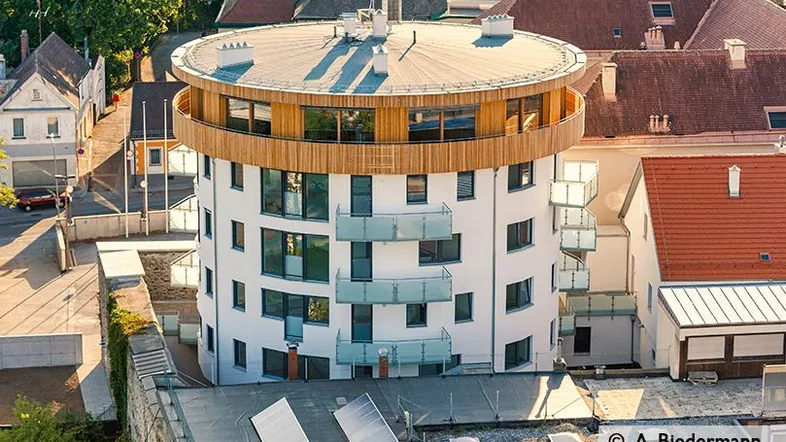 Moderne runde Architektur mit Holzfassade und Balkonen, umgeben von Wohngebäuden.