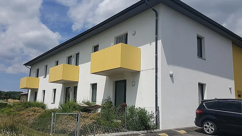 Modernes Mehrfamilienhaus mit weißer Fassade, gelben Balkonen und Satteldach unter blauem Himmel.
