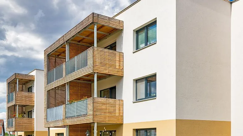 Moderne Wohngebäude mit hellen Fassaden und Holzverkleidung an den Balkonen unter blauem Himmel.
