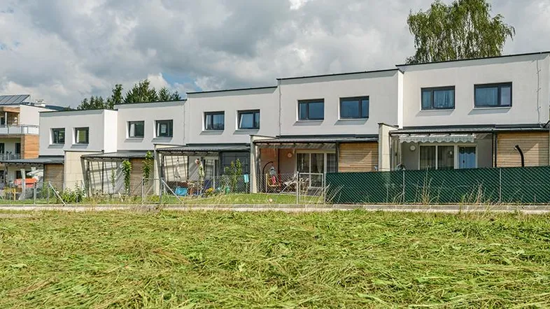 Reihe moderner Reihenhäuser mit kleinen Gärten und Terrassen, umgeben von Grünflächen.