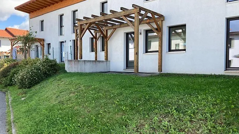 Weißes Reihenhaus mit Holzpergola und kleiner Rasenfläche im Vorgarten, ideal für Entspannung.