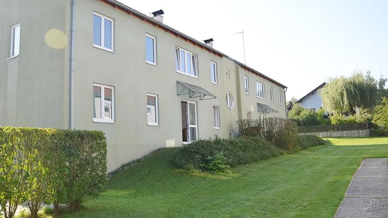Grünes Mehrfamilienhaus mit gepflegtem Rasen und Hecke in ländlicher Umgebung.