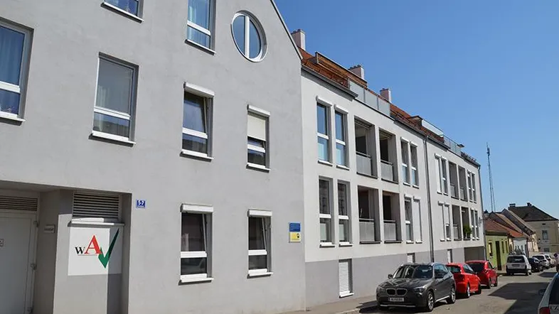 Ansicht der modernen Wohnhausfassade mit Fenstern und Rollläden entlang einer ruhigen Straße.