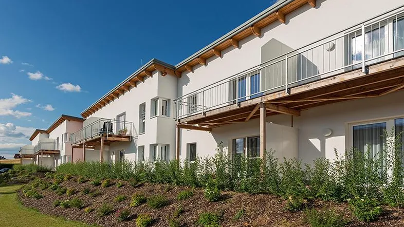 Moderne Reihenhausfassade mit Balkonen, gepflegtem Gartenbereich und blauem Himmel.
