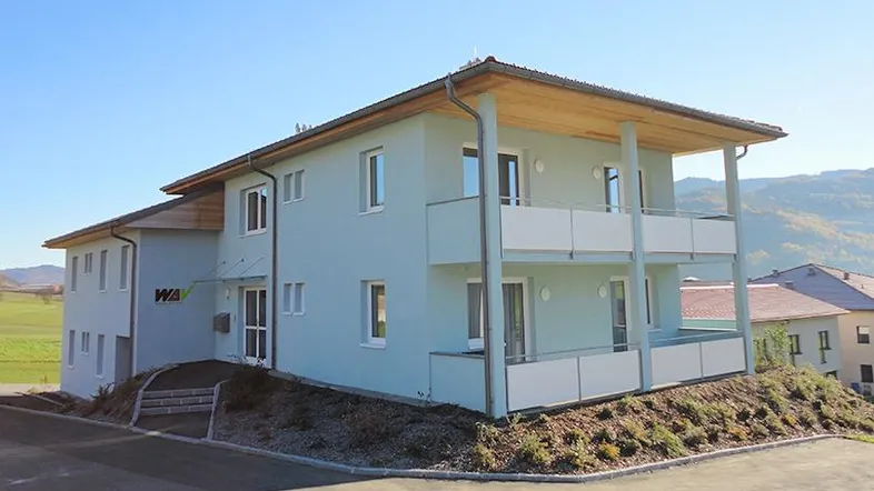 Modernes Gebäude mit hellblauer Fassade, Balkonen und Blick auf die umliegende Landschaft.