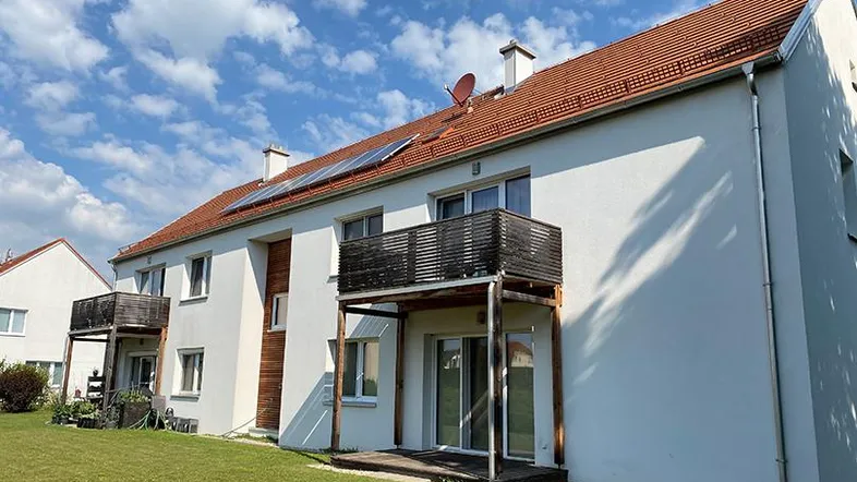 Mehrfamilienhaus mit weißer Fassade, roten Ziegeldächern, Balkonen und Photovoltaikanlage auf dem Dach.